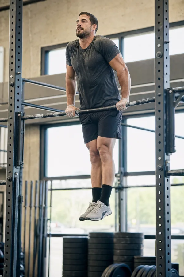 CrossFit athlete finishing a bar muscle-up above a pull-up rig in a gym