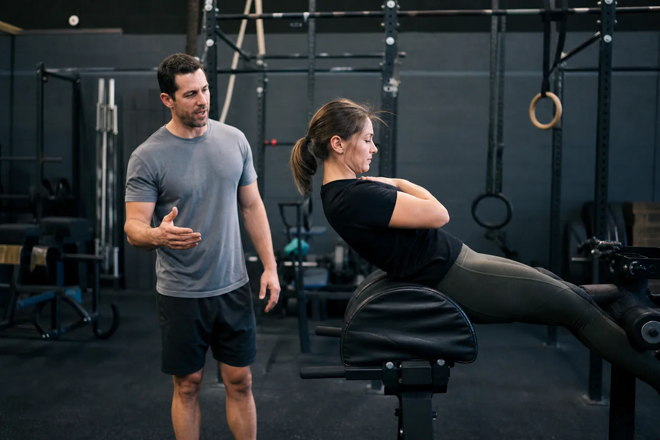 CrossFit athlete practicing a shortened range GHD sit-up progression with coach supervision