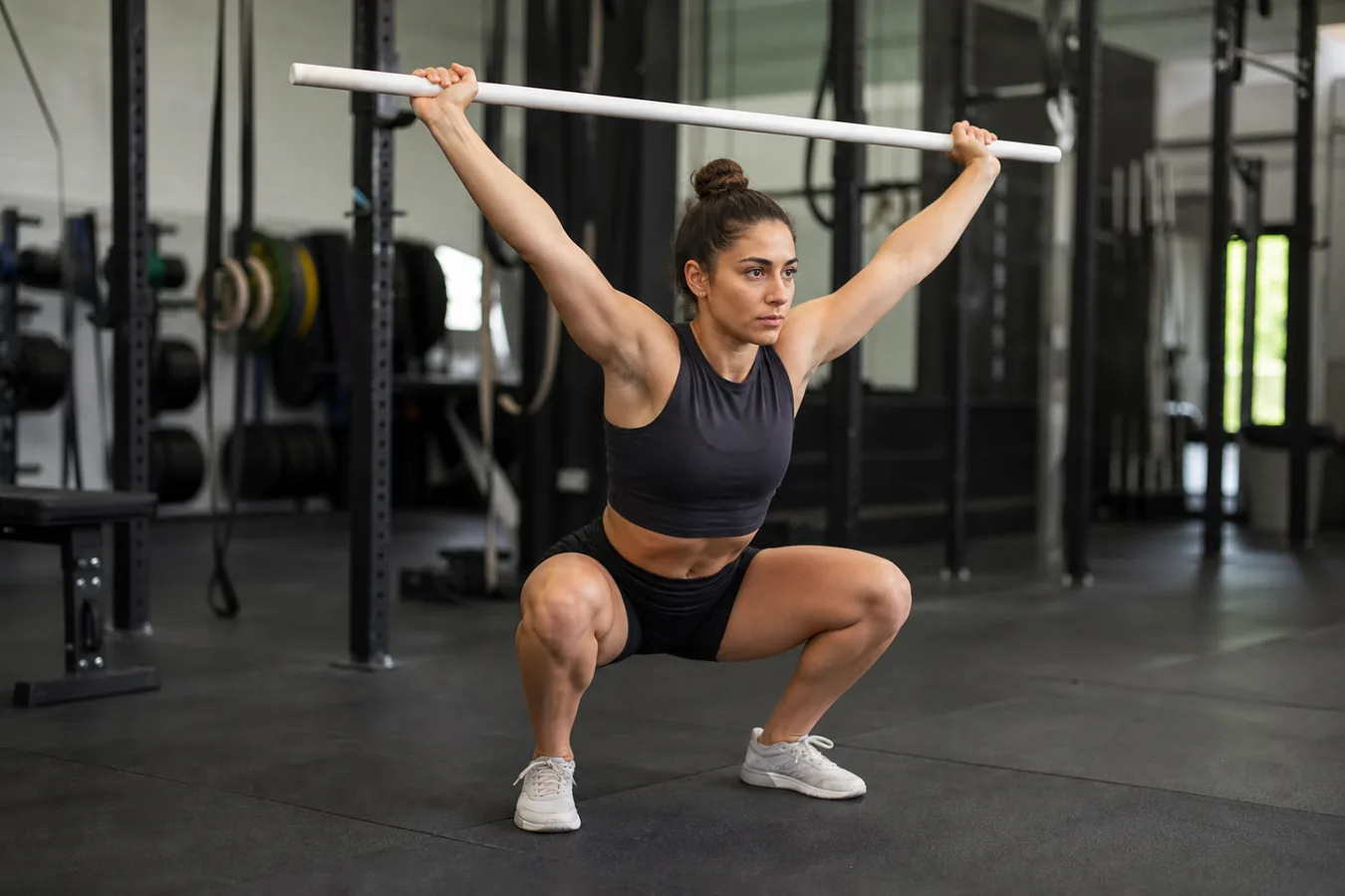 Athlete practicing overhead squat mobility with a PVC pipe in a gym