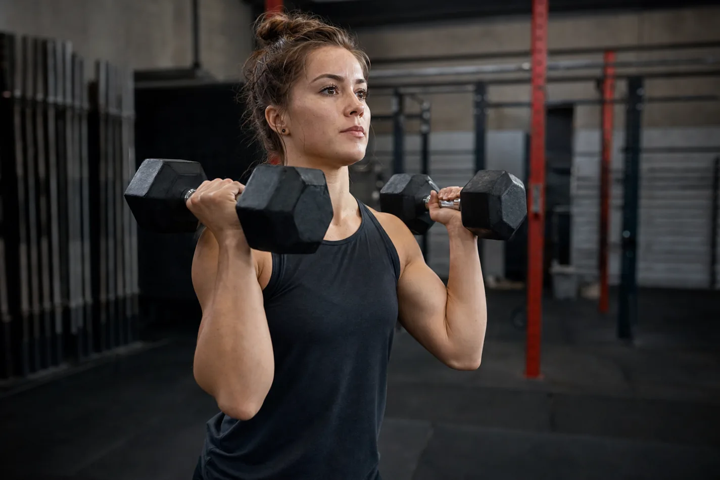 CrossFit athlete holding two dumbbells in a strong front rack before a thruster