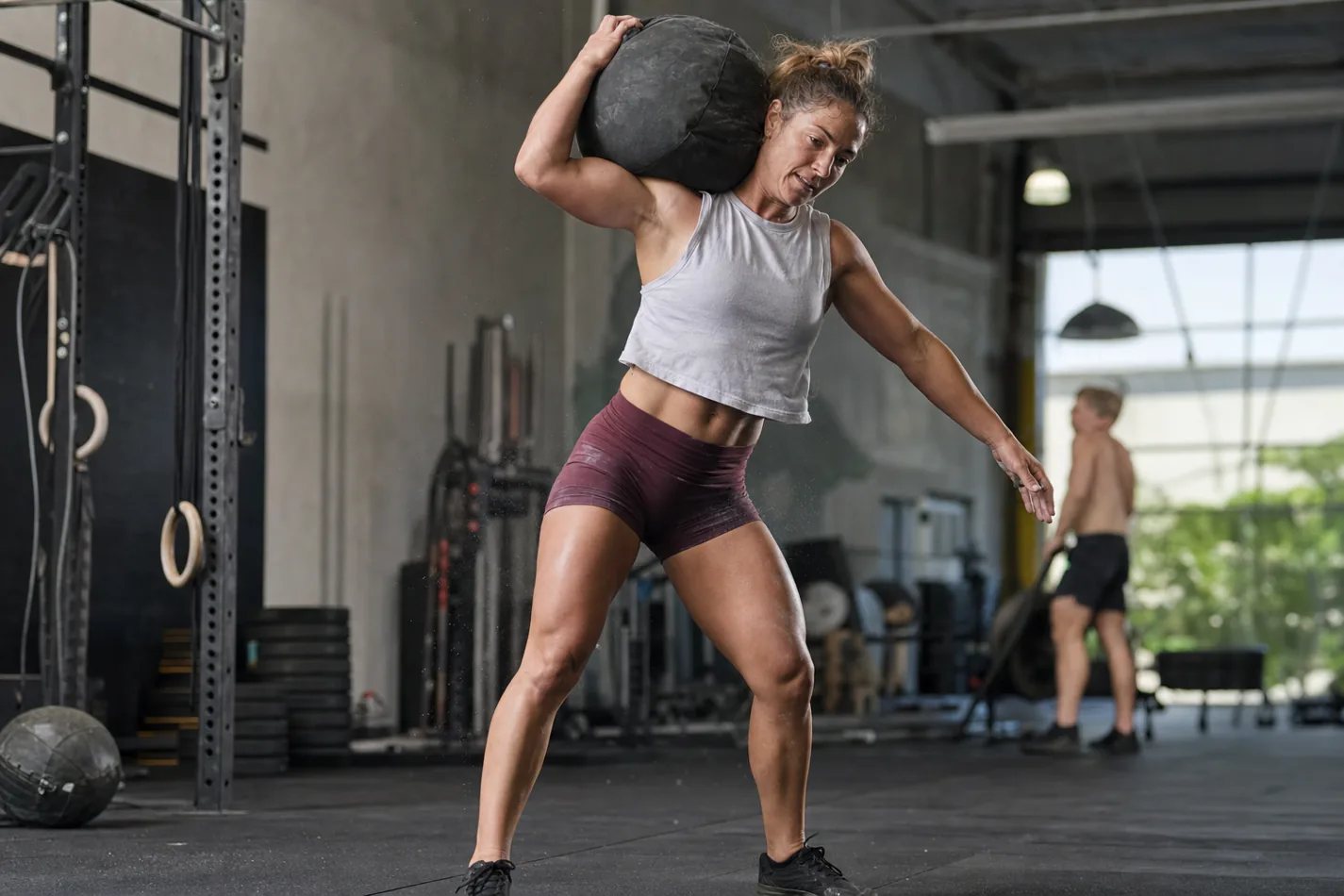 CrossFit athlete finishing a D-ball over shoulder rep with strong hip extension
