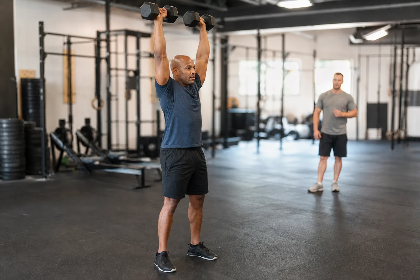 CrossFit athlete finishing a dumbbell thruster overhead with a stable lockout