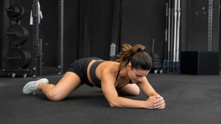 CrossFit athlete demonstrating a controlled frog stretch on a gym floor