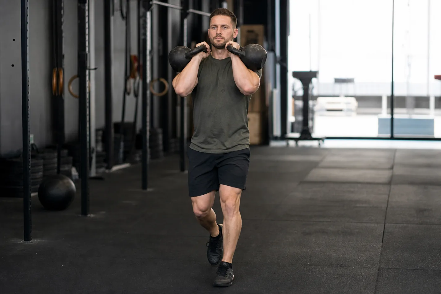 CrossFit athlete walking with two kettlebells in the front rack position