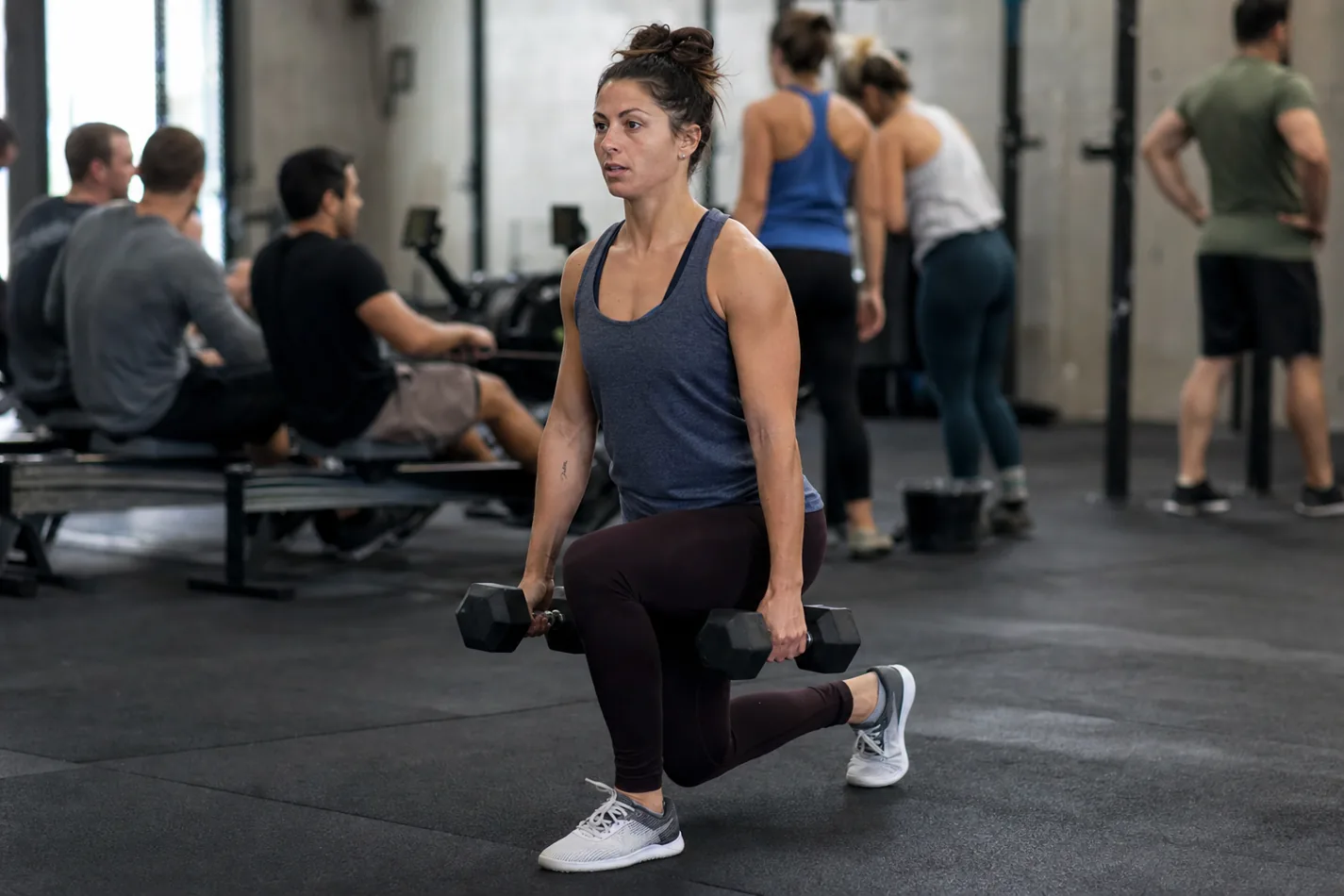 CrossFit athlete doing alternating dumbbell reverse lunges during a class workout