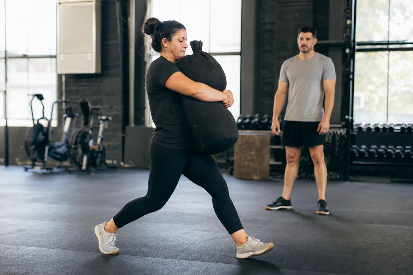 CrossFit athlete carrying a sandbag in a bear hug during a workout