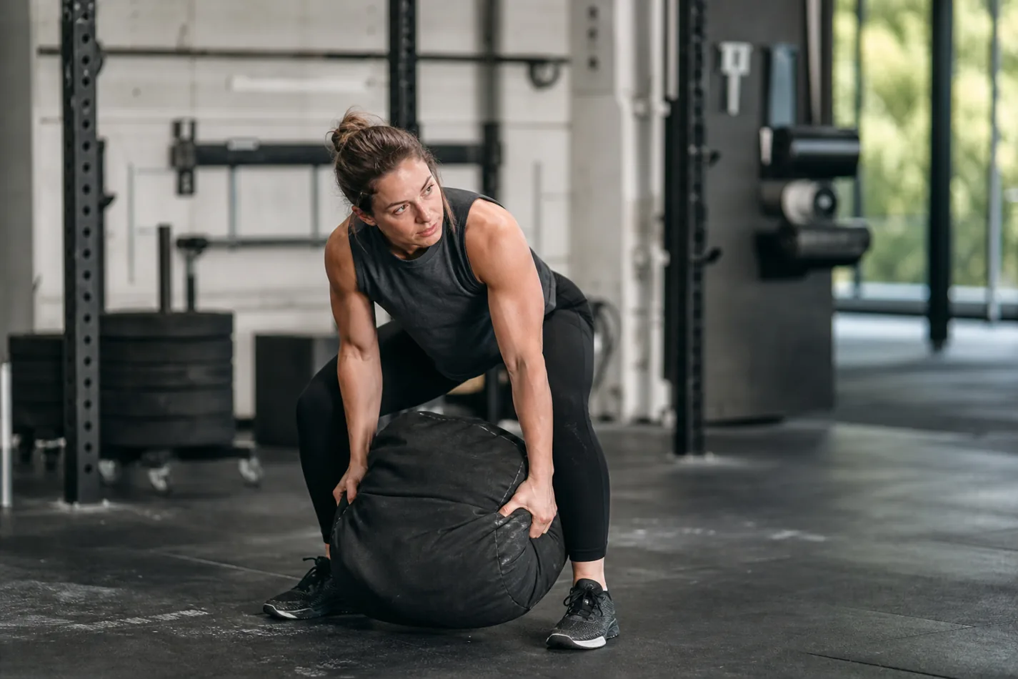 Athlete lifting a heavy sandbag over the shoulder in a CrossFit gym
